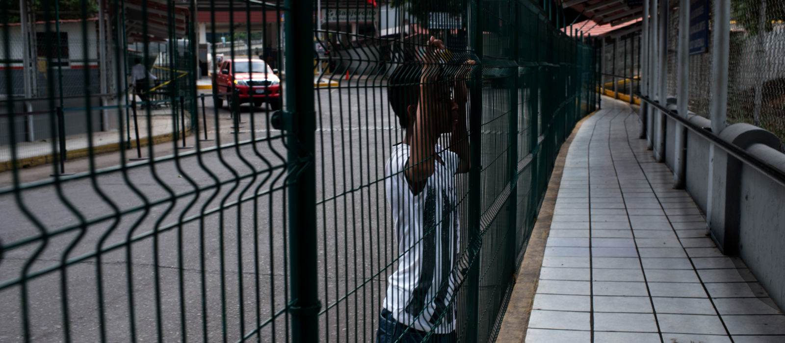 The picture at the border between Mexico and Guatemala. A boy is looking through the fence.