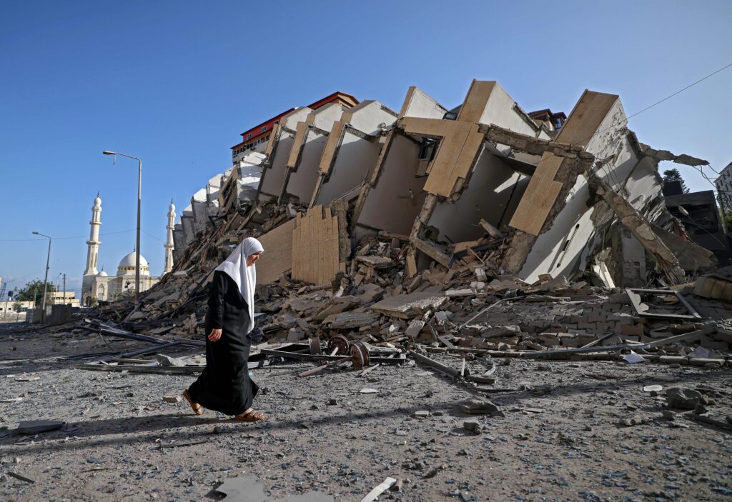 A Palestinian woman walks past a destroyed building in Gaza City early on May 12, 2021, as Hamas militants and the Israeli army exchanged a barrage of deadly fire in the early hours of the day with intense fighting continuing for the second day in a row. - Israeli air raids in the Gaza Strip have hit the homes of high-ranking members of the Hamas militant group, the military said Wednesday, with the territory's police headquarters also targeted. (Photo by MOHAMMED ABED / AFP) (Photo by MOHAMMED ABED/AFP via Getty Images)