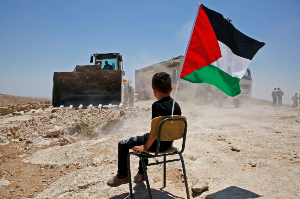 A Palestine boy sits on a chair with a national flag as Israeli authorities demolish a school site in the village of Yatta, south of the West Bank city of Hebron and to be relocated in another area, on July 11 2018.