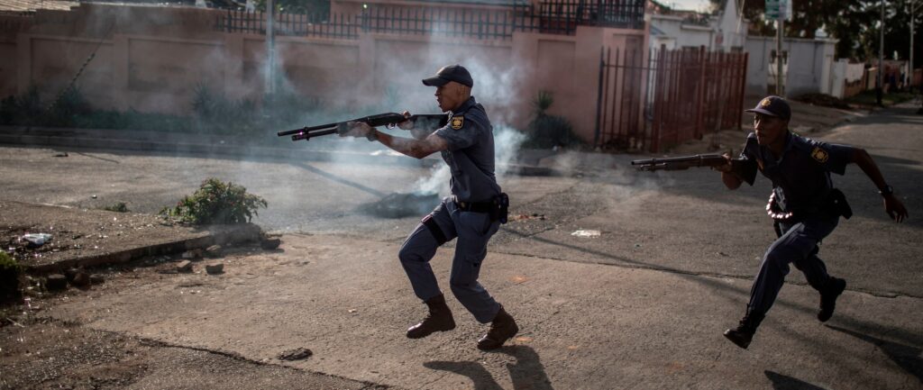 South African police officers fire rubber bullet as they chase protestors in the streets of Johannesburg, on April 23, 2019 during a protest against the lack of service delivery or basic necessities such as access to water and electricity, housing difficulties and lack of public road maintenance. - Police and protesters exchanged volleys of teargas and stones in Johannesburg on April 23, 2019 after a suburb erupted into protest over public services ahead of polls on May 8. Dozens of residents in the working class Turffontein suburb blocked the main road through ward 55, burning tyres, mattresses and tree branches over allegedly unfair allocation of nearby new social housing. (Photo by MARCO LONGARI / AFP) (Photo by MARCO LONGARI/AFP via Getty Images)