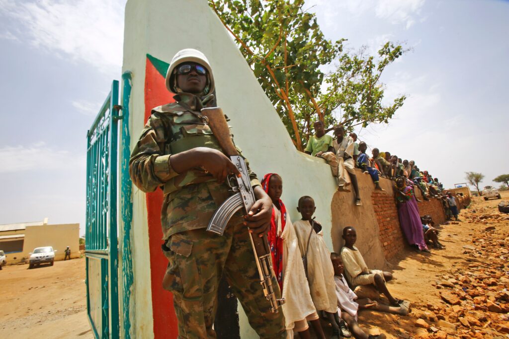 A UN peacekeeper stands guard as crowds of children and villagers gather to welcome Steven Koutsis (unseen), the United States' top envoy in Sudan, in the war-torn town of Golo in the thickly forested mountainous area of Jebel Marra in central Darfur on June 19, 2017. The town was a former rebel bastion which was recently captured by Sudanese government forces. The top US envoy in Sudan began a four-day trip to Darfur on June 18, 2017 to assess security in the war-torn region as the UN prepares to downsize its 17,000-strong peacekeeping force. His visit also comes just weeks before President Donald Trump's administration decides whether to permanently lift a two-decades old US trade embargo on Sudan. / AFP PHOTO / ASHRAF SHAZLY