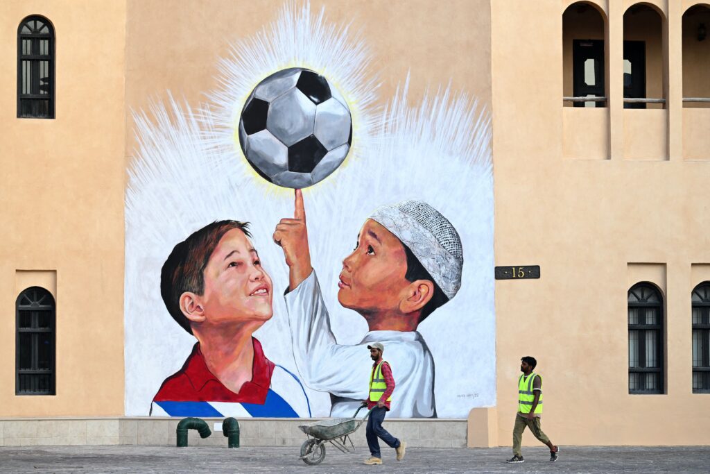 A worker pushes a wheelbarrow past a mural in Doha on November 8, 2022, ahead of the Qatar 2022 FIFA World Cup football tournament. (Photo by Gabriel BOUYS / AFP) (Photo by GABRIEL BOUYS/AFP via Getty Images)
