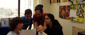 A group of telemarketing agents sitting at desk, wearing headsets and discussing campaigns.